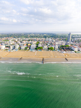 Aerial view of the sandy beach with rows of umbrellas, turquoise sea, and urban buildings in Lido di Jesolo, Veneto, Italy.