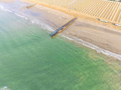 Aerial view of the sandy beach at Lido di Jesolo with rows of parasols, a wooden pier extending into the turquoise sea, and gentle waves, Lido di Jesolo, Veneto, Italy.