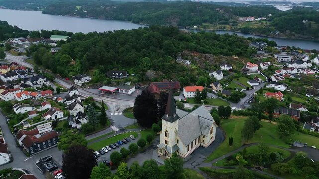 Aerial view of the historic Grimstad Church surrounded by lush greenery and residential houses in the coastal town of Grimstad, Agder, Norway.