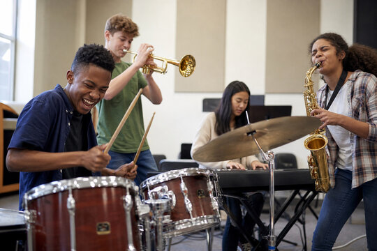 Diverse group of young musicians plays in a bright rehearsal space, drums, trumpet, saxophone, and keyboard energizing the scene with teamwork.