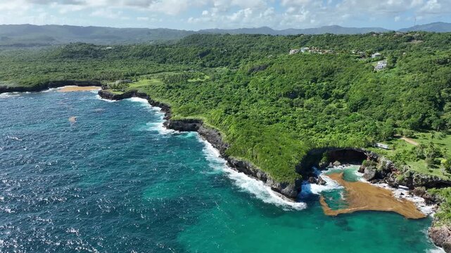 Aerial view of the lush green coastline, rocky cliffs, and turquoise waters of a secluded cove in Las Terrenas, Samana Province, Dominican Republic.