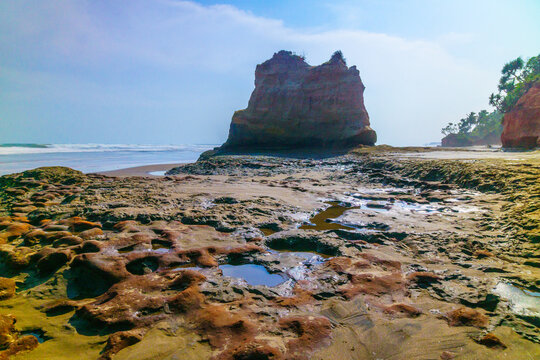 View of the unique coastal rock formation at Lais beach, featuring tide pools, sandy shoreline, and ocean waves under a clear blue sky in Lais, Bengkulu, Indonesia.