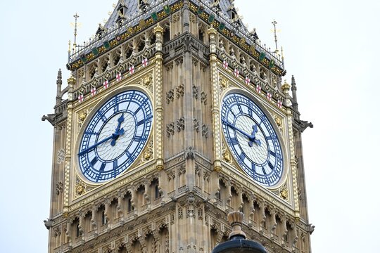 View of Big Ben clock tower featuring intricate gothic architecture, golden details, and blue clock faces against a bright sky in London, England, United Kingdom.