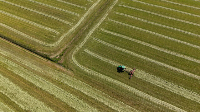 Aerial view of a tractor tedder working on freshly cut grass, turning and spreading hay evenly to improve drying in Milan, Lombardy, Italy.