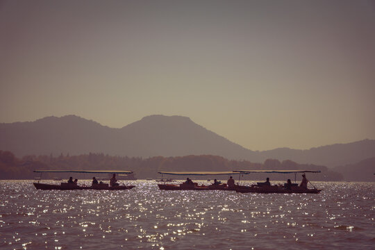 View of traditional boats with people on the shimmering water of West Lake with mountains in the background in Hangzhou, China.