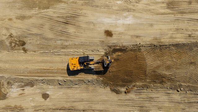 Aerial view of a yellow excavator working on a railway construction site with piles of earth and tracks in Milan, Lombardy, Italy.