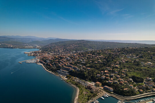 Aerial view of the coastal town of Muggia, featuring its marina, residential buildings, and lush green hills along the Adriatic Sea in Trieste, Friuli-Venezia Giulia, Italy.