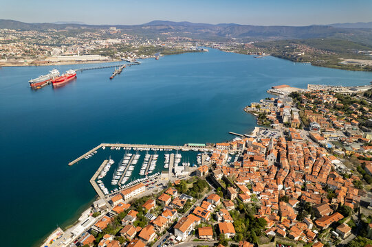 Aerial view of the historic town of Muggia with its terracotta rooftops, marina filled with sailboats, and the blue waters of the Gulf of Trieste in Trieste, Friuli-Venezia Giulia, Italy.