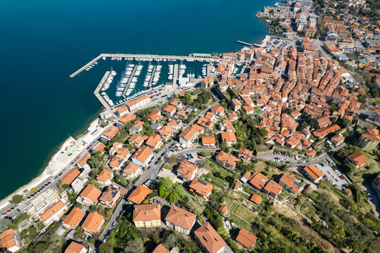 Aerial view of the historic town of Muggia with its terracotta rooftops, marina filled with boats, and coastal setting in Trieste, Friuli-Venezia Giulia, Italy.