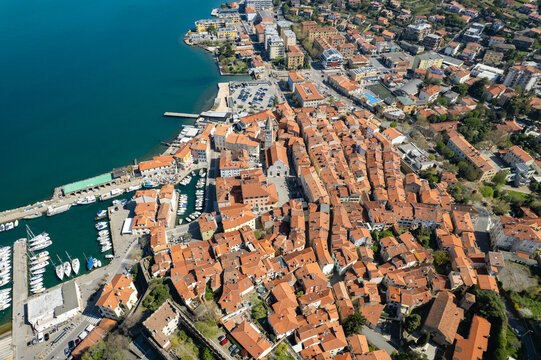 Aerial view of the historic town of Muggia with its harbor, boats, and dense terracotta rooftops along the Adriatic coast in Trieste, Friuli-Venezia Giulia, Italy.