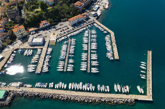 Aerial view of Muggia marina filled with numerous sailboats docked at the piers along the coast in Trieste, Friuli-Venezia Giulia, Italy.