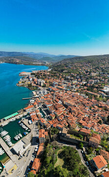 Aerial view of the historic town of Muggia with terracotta rooftops, harbor filled with boats, and coastal landscape along the Adriatic Sea in Trieste, Friuli-Venezia Giulia, Italy.