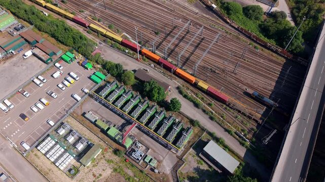 Aerial view of industrial compressor units and power generators near a busy rail yard with freight trains and a parking lot in Doncaster, England, United Kingdom.