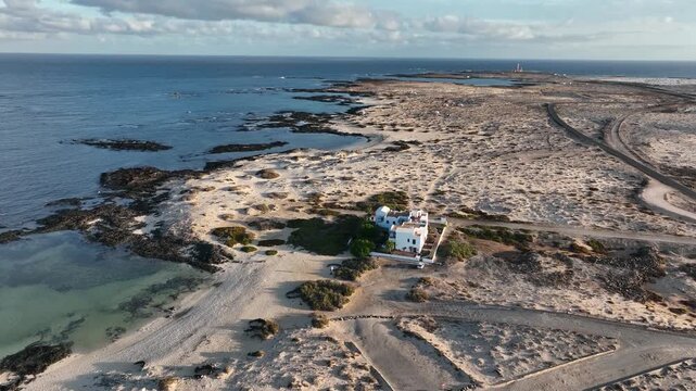 Aerial view of Faro de Toston lighthouse surrounded by rugged volcanic terrain and the blue Atlantic Ocean in La Oliva, Canary Islands, Spain.