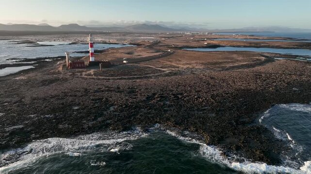 Aerial view of Faro de Toston lighthouse on the rocky volcanic coastline of Fuerteventura surrounded by the Atlantic Ocean in La Oliva, Canary Islands, Spain.