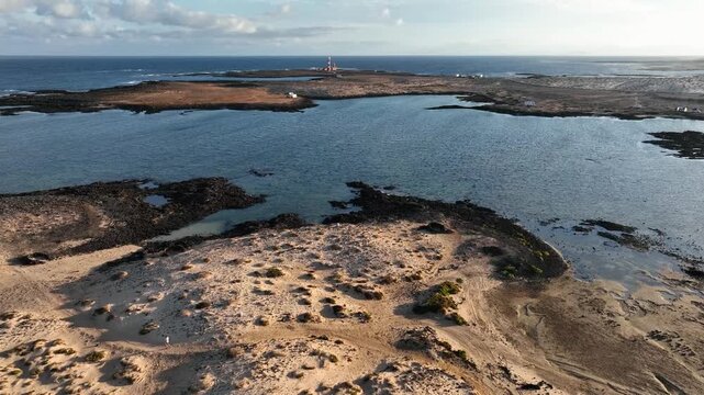 Aerial view of Faro de Toston lighthouse surrounded by sandy dunes and blue ocean waters in La Oliva, Canary Islands, Spain.