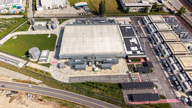 Aerial view of a modern data center facility featuring industrial buildings, solar panels, and surrounding infrastructure in Settala, Lombardy, Italy.