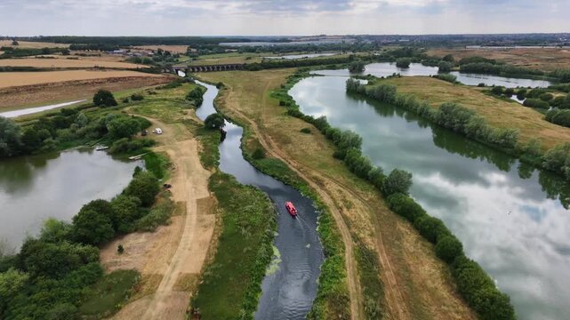 Aerial view of the River Nene with a small boat navigating the winding waterway through green fields and rural landscape in England, United Kingdom.