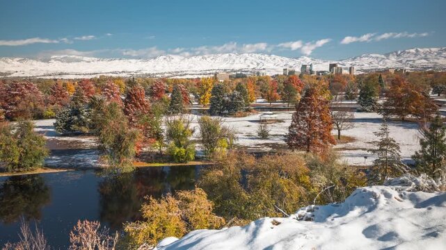 Aerial view of Ann Morrison Park featuring snow-covered trees, a pond, and the Boise city skyline against a backdrop of snow-capped mountains in Boise, Idaho, United States.