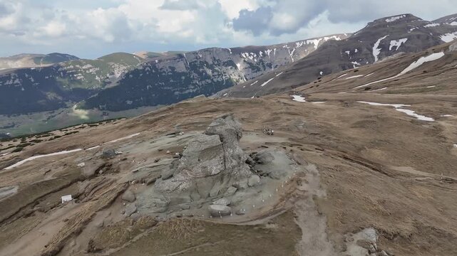 Aerial view of the Sphinx rock formation surrounded by rugged mountain terrain, hiking trails, and patches of snow in the Bucegi Mountains, Sinaia, Prahova, Romania.