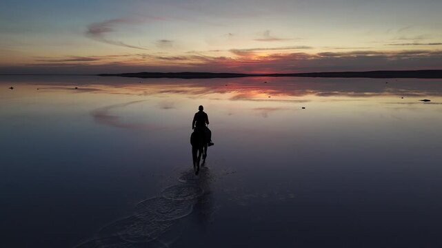 Aerial view of a person riding a horse on the reflective surface of Lake Tuz at sunset in Kulu, Konya, Turkiye.