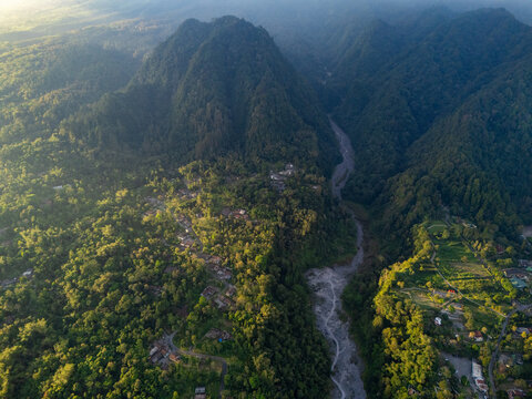 Aerial view of Turgo mountain surrounded by dense tropical forests, a winding river valley, and a small village in Pakem, Special Region of Yogyakarta, Indonesia.