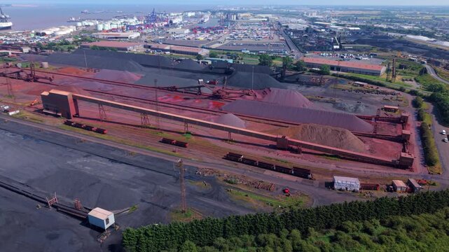 Aerial view of Immingham Bulk Terminal with large stockpiles of iron ore and coal, conveyor systems, and railway infrastructure in South Killingholme, England, United Kingdom.