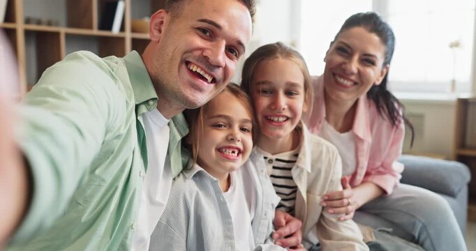 Family parents children selfie home smartphone together portrait. Smiling and happy faces relax on a cozy sofa, capturing candid bonding and joy. Ideal concept of warm family unity values.