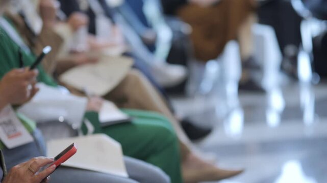 People sit in waiting area, checking phones. Some hold documents, others relax. Focus on hands and devices. Ideal for travel, airport, or event waiting scenes