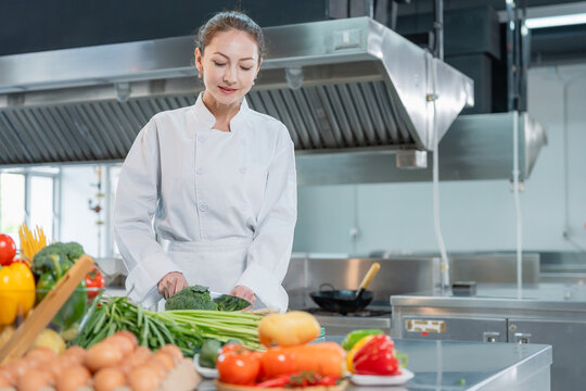 Professional female chef cutting vegetables in commercial kitchen, Smiling woman chef preparing fresh food in restaurant kitchen, Chef cooking healthy meal with fresh vegetables in kitchen