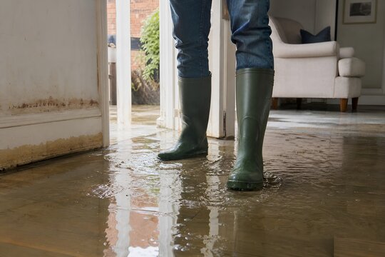 Person Wearing Rubber Boots Standing in a Flooded Home Interior During Heavy Rain