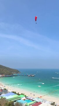 Aerial view of a red parasail flying high in the clear blue sky over a beautiful tropical beach and turquoise ocean.
