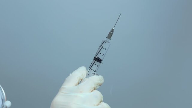 Clinician wearing latex glove holding medical syringe with fluid dose for weight management injection treatment on blue background
