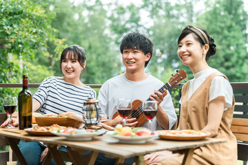 Obraz premium Young Asian men and women, friends, colleagues, and coworkers enjoying a barbecue, home party, and glamping on a wooden deck.