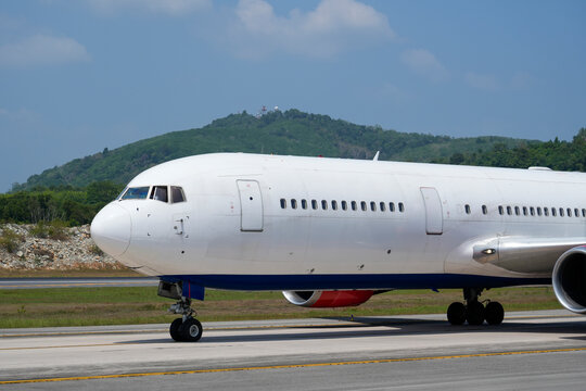 Commercial passenger airplane moving slowly on the concrete tarmac at an airport with a scenic mountain range under a clear blue sky