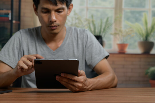 Young man using tablet device at wooden table in bright indoor space with plants