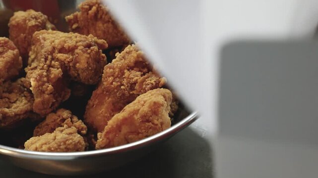 그릇에 담긴 바삭하게 튀겨진 후라이드 치킨 조각들을 집게로 집어 올리는 모습