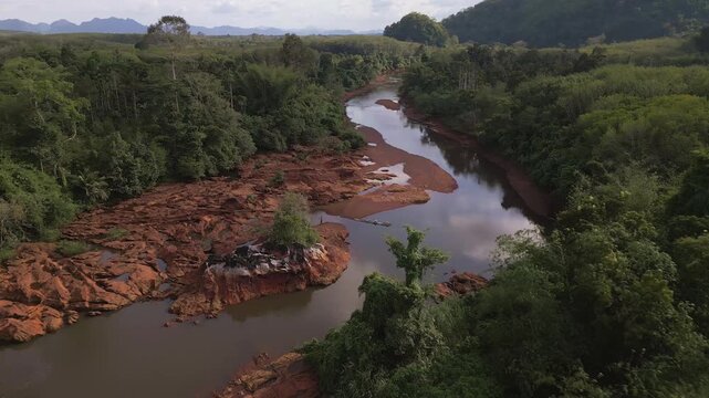Red rock river bed aerial panning view near Khao Sok National Park with water reflecting the clouds and blue sky  in Surat Thani, Thailand