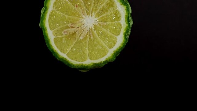 Sliced kaffir lime on black background with water drop.