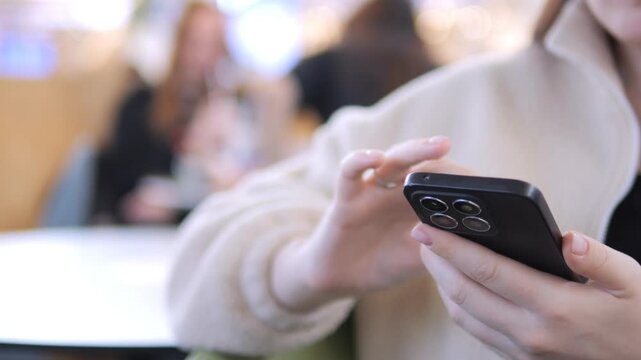 Person holds phone, taps screen with focus. Hands show detailed interaction. Background blurred, indoor setting. Could be used for digital communication, social media, or technology concepts