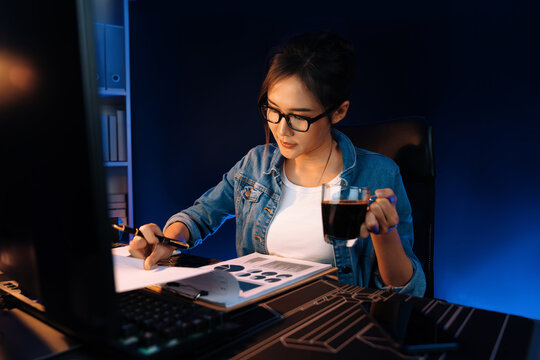 Creating young beautiful Asian creative woman thinking of sales target report on business market graph folder paperwork report, looking out of indoor with holding pen at neon at night time. Stratagem.