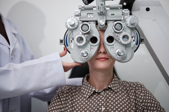 Close-up, female patient eye exam with phoropter equipment, vision and eyesight improvement by expert optometrist, diagnostic for eyeglasses lens, professional technology services in optical clinic.