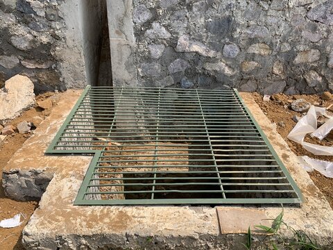 Steel drain grate covering a concrete drainage channel in an outdoor infrastructure setting.