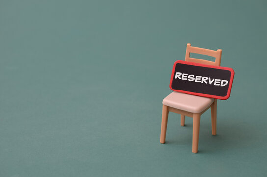 Miniature chair with reserved sign on green background for business booking and vacancy concept