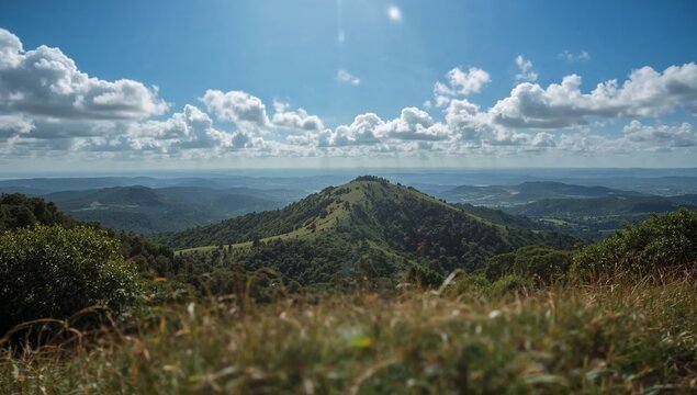 Panoramic view of rolling green hills under a bright blue sky with fluffy clouds.
