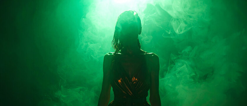 Portrait of a mysterious woman in glowing emerald green smoke and dramatic neon backlighting. Perfect for moody conceptual stock phot