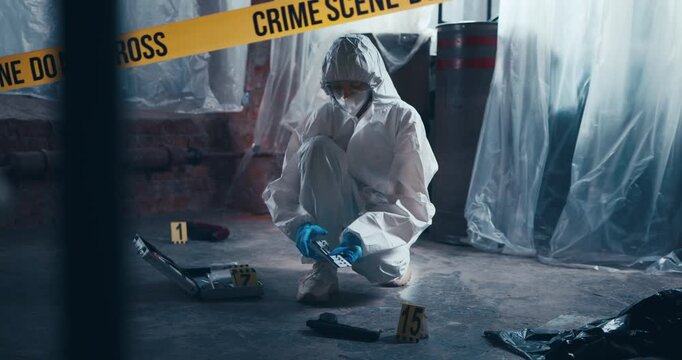 Forensic specialist places an evidence marker and measuring scale beside a handgun during crime scene documentation.