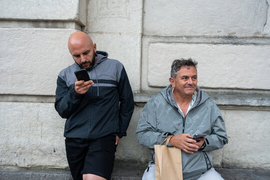 Two men waiting outdoors using smartphones