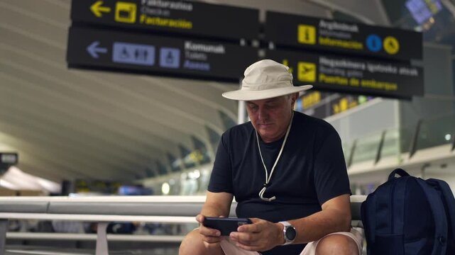 Mature tourist man watching video on smartphone at airport