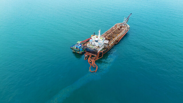 Oil spill Industrial response ship deploying an orange containment boom to control and clean up a marine pollution spill in the open ocean, protecting the sea ecosystem from hazardous chemical waste.